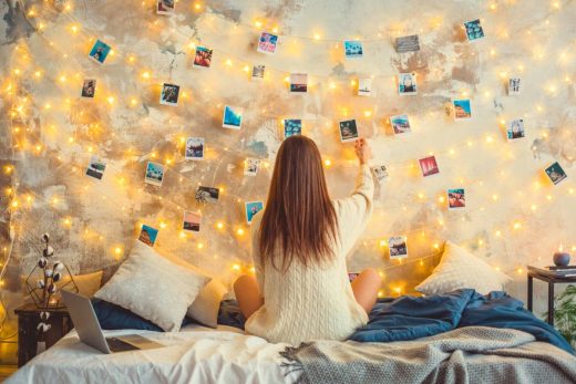 adolescente sur son lit accroche des photos sur un mur avec des guirlandes