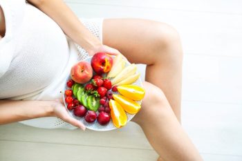 Jeune femme très enceinte avec assiette de fruits