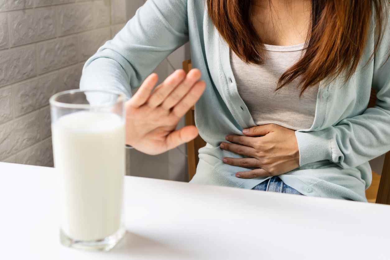 une femme fait un signe stop de la main devant un verre de lait, mal au ventre, concept d'intolérance au lactose